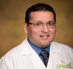 Headshot of Dr. Boris Onate, a family physician for the Center for Living Well - Epcot, wearing a white lab coat and blue button up shirt with a tie