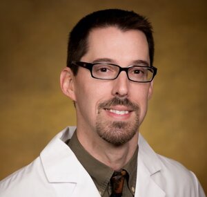 Headshot of Dan Wackerly, pharmacist for the Center for Living Well, wearing a white lab coat and black glasses