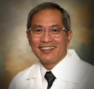Headshot of Dr. Demetrio Suguitan, a board-certified physician for he Center for Living Well - Epcot, wearing a white lab coat and black tie