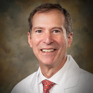 Headshot of Dr. Perry Funk, a board-certified osteopathic family medicine provider for the Center for Living Well - Epcot, wearing a white lab coat and red patterned tie
