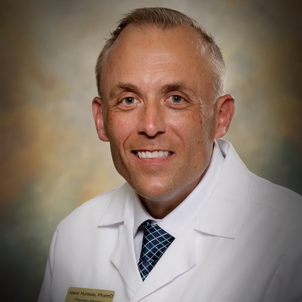 Headshot of Jason Hunkele, Pharmacy Manager for the Center for Living Well - Epcot, wearing g a white lab coat